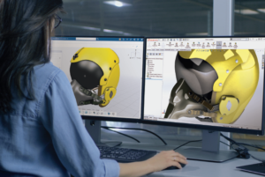 A person seated in front of two computer monitors displaying 3D Sculptor and a 3D model