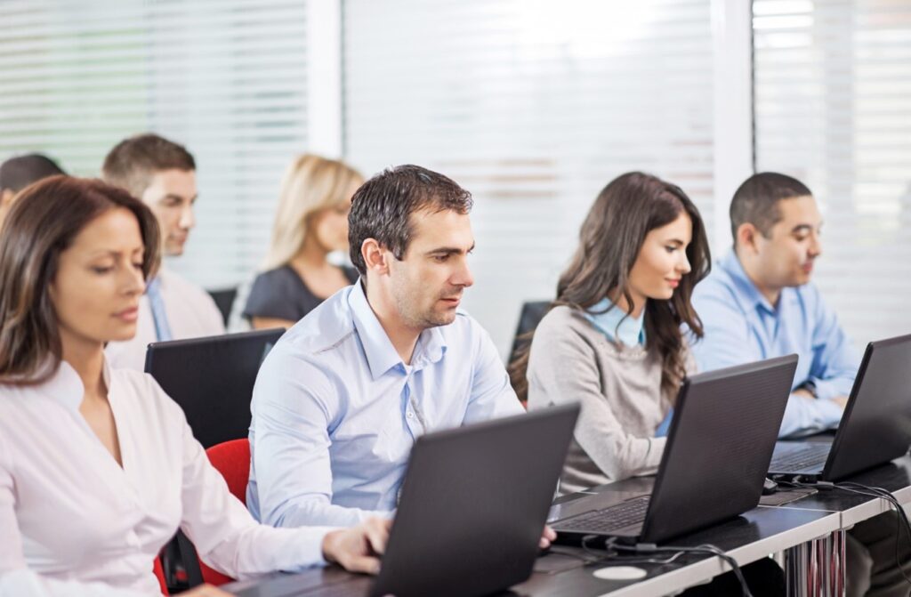 Professionals attending a training session, focused on laptops in a classroom setting, enhancing their technical skills and knowledge.