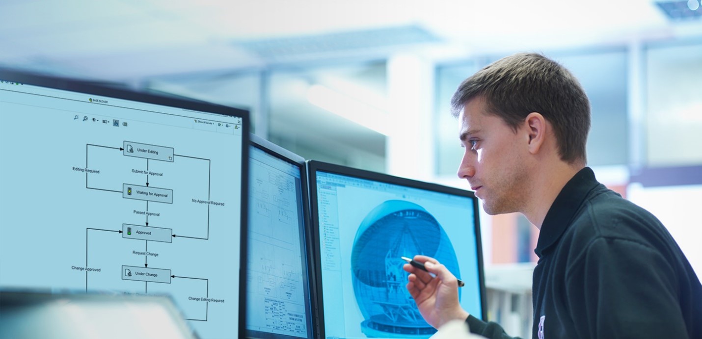 An engineer working on a dual-monitor setup, reviewing a workflow diagram on one screen while analyzing 3D CAD data on the other.